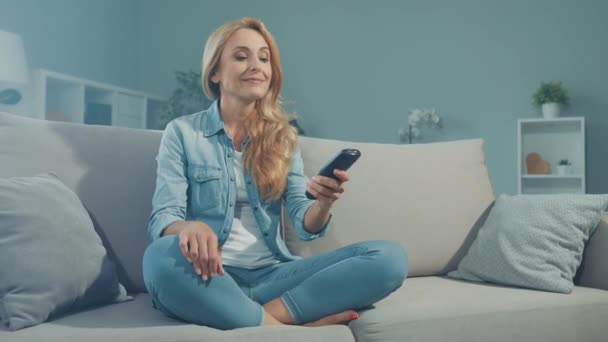 Щаслива приємна смішна леді сидить зручний диван тримайте канал перемикача дистанційного керування — стокове відео