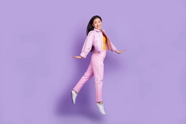 全体形照片甜蜜的千年黑发女士跳跃穿夹克牛仔裤与紫色背景隔离的运动鞋 — 图库照片