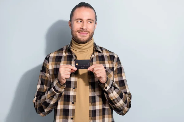 Foto van jonge man bankkaart vroeg zich af kijken lege ruimte doordachte slijtage geruite shirt geïsoleerd over grijze kleur achtergrond — Stockfoto