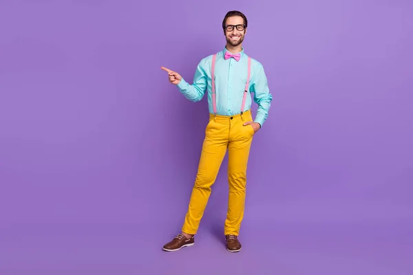 Corpo inteiro foto de fresco millennial morena cara índice vazio espaço desgaste gravata suspensórios camisa óculos calças sapatos isolados no fundo violeta — Fotografia de Stock