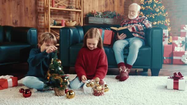 Familie verzamelen traditie kinderen versieren kleine x-mas boom opa ontspannen lezen — Stockvideo