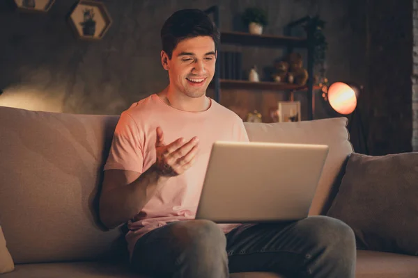 吸引人的开开开心心的男人坐在沙发上的画像 用笔记本电脑打电话给网络交谈联系人 在家里的公寓里交流 — 图库照片