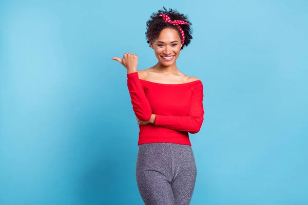 Photo of dreamy sweet afro girl wear off-shoulders red shirt pointing finger empty space smiling isolated blue color background.