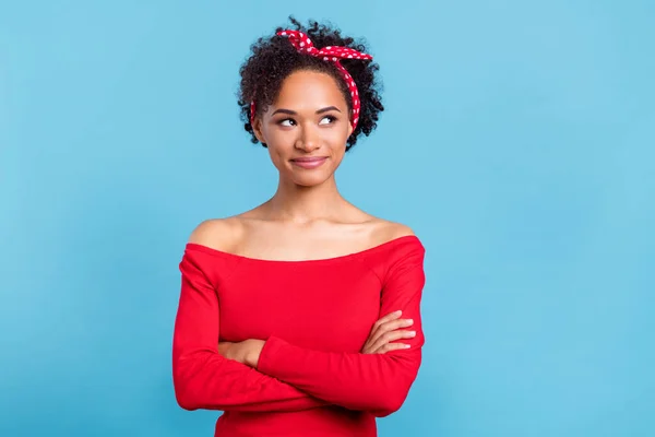 Photo of pretty dreamy afro girl wear off-shoulders red shirt arms crossed looking empty space smiling isolated blue color background.