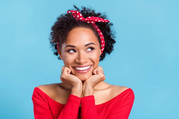 Photo of excited thoughtful afro girl wear off-shoulders red shirt arms cheeks looking empty space smiling isolated blue color background.