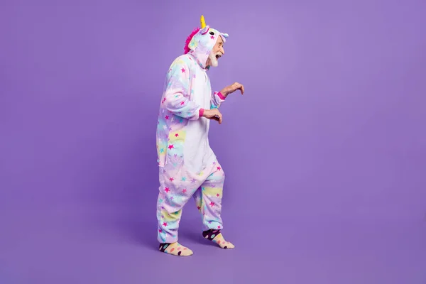 Photo of handsome funny man pensioner unicorn sleepwear dark stealing toes smiling isolated violet color background — Stock Photo, Image