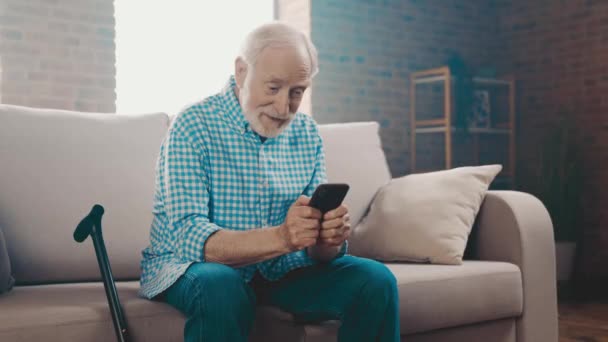 Relaxed modern retired old man sit sofa hold telephone texting relatives — Stock Video