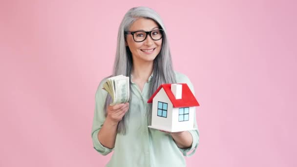 Abuela celebrar casa dinero anuncio comprar oferta aislado pastel color fondo — Vídeos de Stock