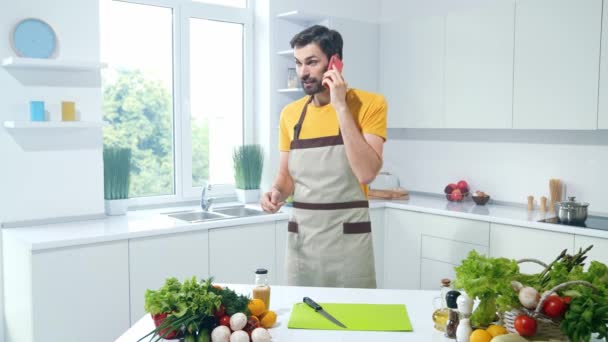 Guy gøre aftensmad salat opskrift forklare kone smart telefonopkald i køkkenet – Stock-video