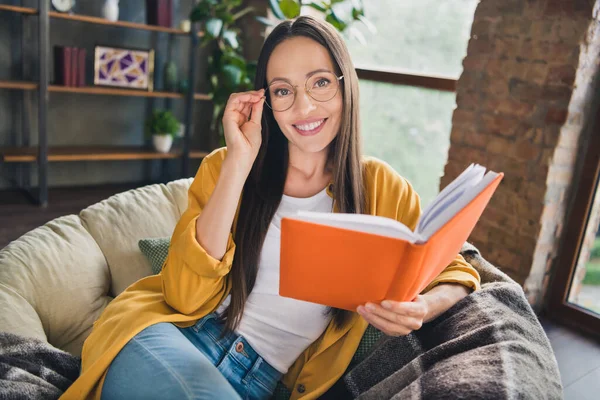 Foto de adorable joven brillante vestido gafas camisa amarilla que descansan leyendo historia sonriendo en el interior habitación casa — Foto de Stock