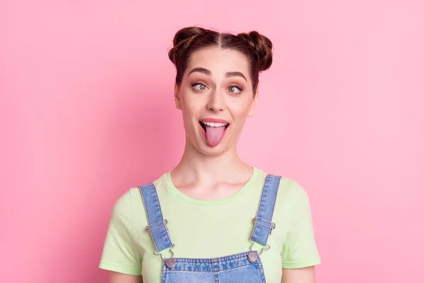 Photo of funky foolish girl grimace crossed eyes protrude tongue wear jeans overall green t-shirt isolated on pink background — Stock Photo, Image