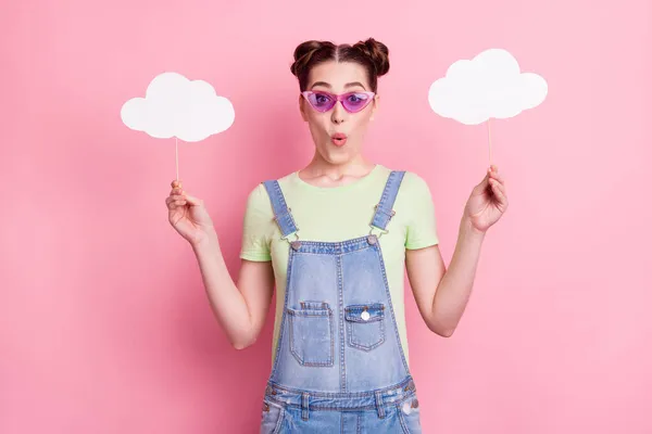 Photo of amazed girl hold two cloud sticks wear sunglass jeans overall green t-shirt isolated on pink background — Stock Photo, Image