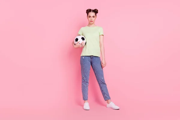 Fotografie de fată încrezătoare ține mingea de fotbal arata camera purta tricou verde blugi încălțăminte izolat pe fundal roz — Fotografie, imagine de stoc