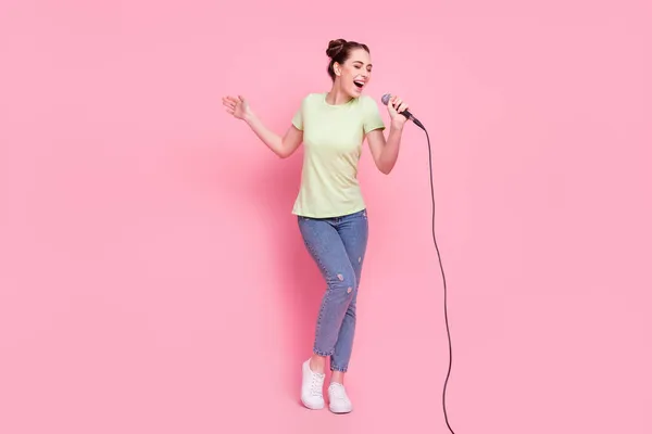Φωτογραφία από ανέμελη τραγουδίστρια κυρία κρατήσει μικρόφωνο τραγουδούν τραγούδι φορούν πράσινο t-shirt τζιν παπούτσια που απομονώνονται σε ροζ φόντο — Φωτογραφία Αρχείου