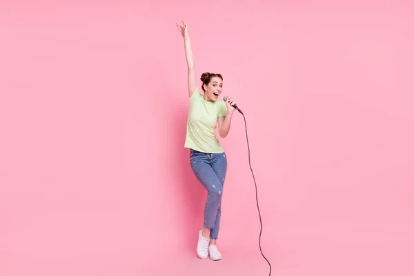 Foto von netten verrückten Dame halten Mikrofon singen heben Hand tragen grünes T-Shirt Jeans Schuhe isoliert auf rosa Hintergrund — Stockfoto
