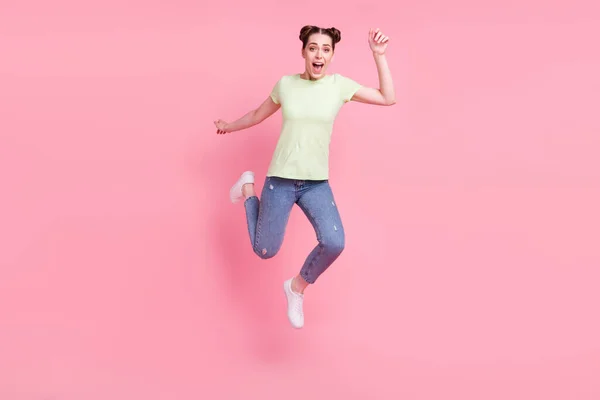 屈託のない素敵な女性のジャンプの写真を実行急いで口を開く緑のTシャツピンクの背景に隔離された着用 — ストック写真