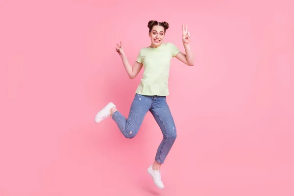 友好而积极的女士跳跃手的照片显示，V字形标志穿着绿色T恤，背景是粉色的 — 图库照片