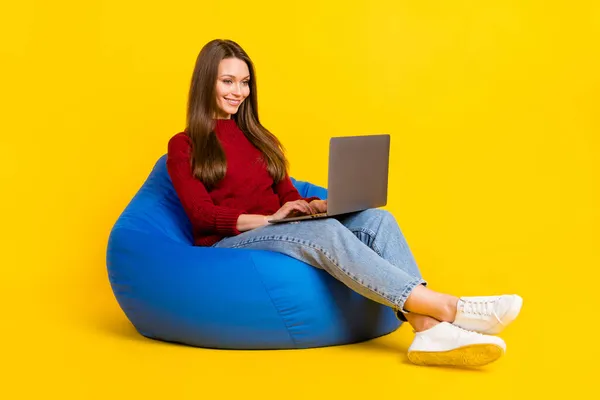 쾌활 한 젊은 여성이 앉아 있는 의자 사진 전체가 밝은 노란색 배경에 고립된 노트북 작업처럼 보인다 — 스톡 사진