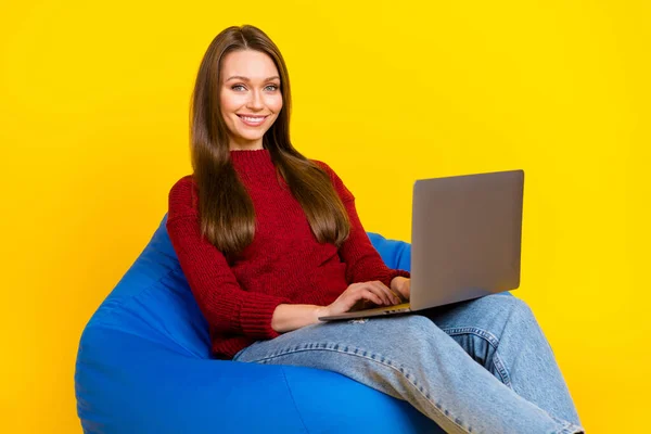 Zdjęcie słodkiej młodej damy siedzieć na torbie pracy laptop nosić sweter dżinsy izolowane na żywy żółty kolor tła — Zdjęcie stockowe