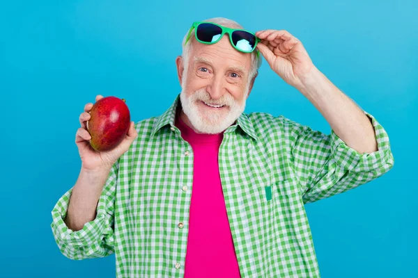 Фото веселого позитивного радісного старого тримає руку манго тропічна фруктова посмішка ізольована на синьому кольорі — стокове фото