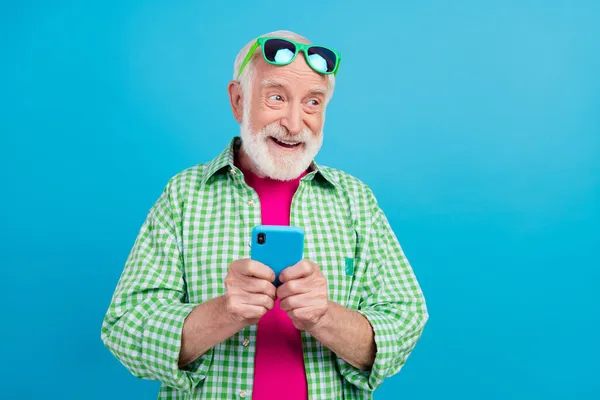 Photo de rêve heureux positif vieux grand-père tenir le téléphone imaginer commentaire média isolé sur fond de couleur bleue — Photo