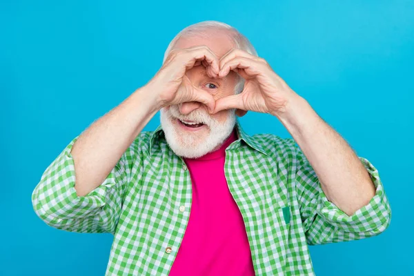Photo de vieux positif heureux homme regard oeil faire doigts petit coeur forme sourire isolé sur fond de couleur bleue — Photo