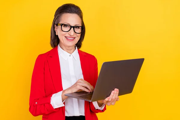 Fotografie učitele starší bruneta dáma držet notebook nosit brýle červená svetr izolované na žluté barvy pozadí — Stock fotografie