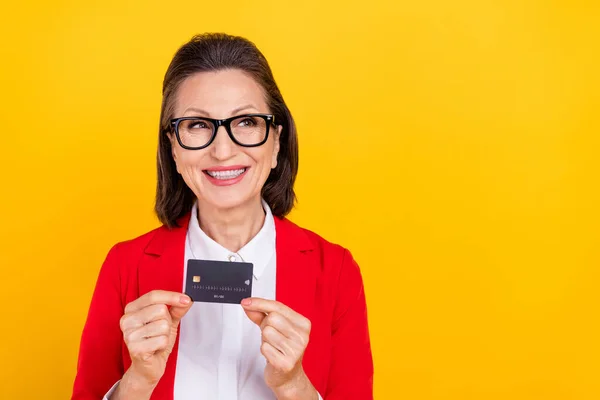 Foto de hr senhora morena envelhecida com cartão olhar promo desgaste óculos vermelho cardigan isolado no fundo de cor amarela — Fotografia de Stock