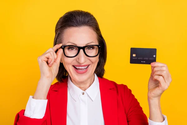 Foto de funky envelhecido morena senhora segurar cartão desgaste óculos vermelho casaco isolado no fundo de cor amarela — Fotografia de Stock