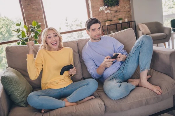 Fotografie atraktivní šťastný mladý pár nosit ležérní oblečení usměvavý sedací gauč hrát hru Playstation uvnitř domu pokoj — Stock fotografie