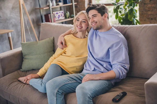 Retrato de atractiva pareja alegre sentada en diván abrazando viendo series de programas de televisión en casa loft interior industrial en interiores — Foto de Stock
