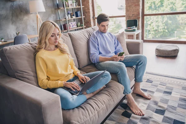 Foto de comprimento total do jovem casal uso navegar celular laptop on-line sentar sofá fim de semana livre dentro de casa — Fotografia de Stock