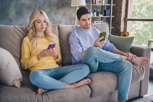 Retrato de atraente casal viciado focado sentado no divã usando dispositivo gadget conversando em casa loft interior industrial dentro de casa — Fotografia de Stock