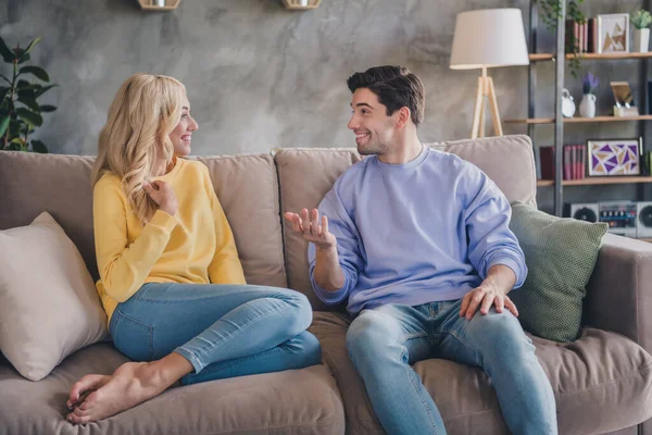 Foto de pareja joven bastante linda usar trajes casuales sonriendo sofá sentado comunicándose en el interior habitación de la casa — Foto de Stock