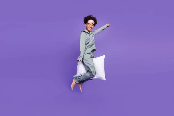 Foto bonita atraente Africano senhora cinza nightwear sorrindo saltando alta equitação travesseiro isolado roxo cor fundo — Fotografia de Stock