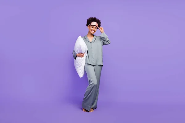 Photo charming cute african lady grey nightwear smiling holding pillow arm hand mask isolated purple color background.
