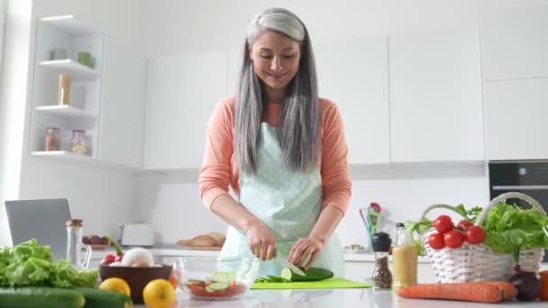 Изысканные дамы среднего возраста делают потерю веса ужин вырезать огурец на кухонном столе — стоковое видео