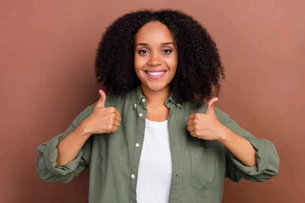 Foto de morena legal jovem afro penteado senhora mostrar polegar para cima usar camisa militar isolado no fundo de cor marrom — Fotografia de Stock