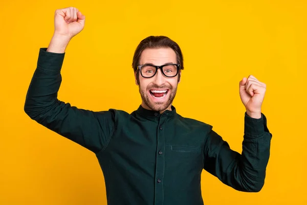 Фото возбужденного смешного молодого человека носить умные очки повседневной одежды поднимая кулаки улыбаясь изолированный желтый цвет фона — стоковое фото