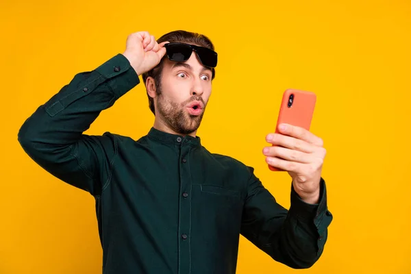 Fotografie šokovaného ohromený mladý chlap oblečený inteligentní ležérní oblečení rameno tmavé brýle čtení moderní gadget izolované žluté barvy pozadí — Stock fotografie