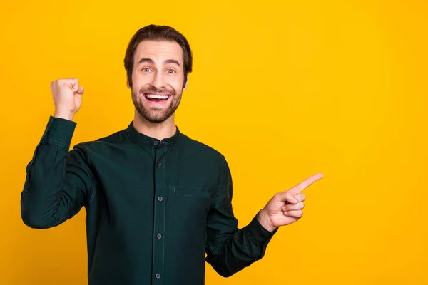 Foto av glada lycklig ung kille klädd smart casual kläder ler stigande knytnäve peka finger tomt utrymme isolerad gul färg bakgrund — Stockfoto