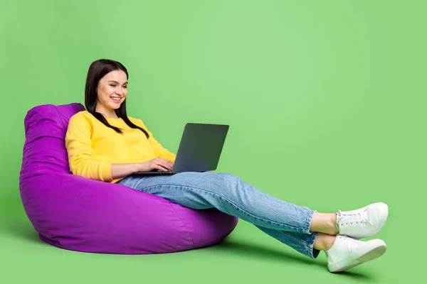 Tampilan ukuran tubuh penuh dari gadis ceria yang duduk di kursi tas menggunakan laptop yang menyenangkan dan terisolasi dari latar belakang warna hijau — Stok Foto