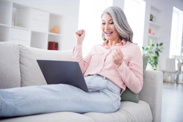Фото ура волнистая прическа леди в возрасте смотреть ноутбук носить розовую рубашку джинсы сидеть дома в одиночестве — стоковое фото