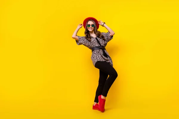 Фотография в полный рост очаровательной счастливой привлекательной молодой женщины в красной шляпе, изолированной на желтом цветном фоне — стоковое фото