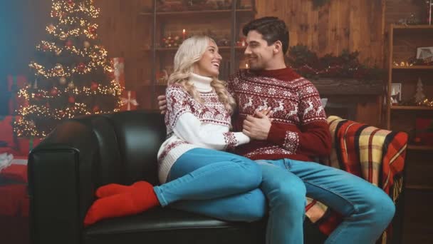 Lady srác ül hangulatos kanapé ölelés szilveszter fa x mas print pulóver fények beltérben — Stock videók