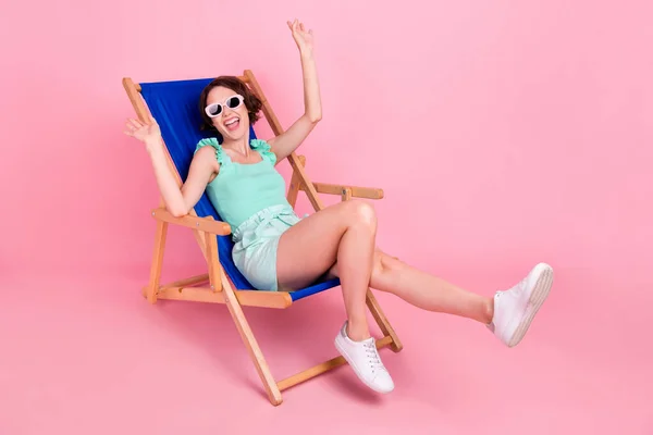 Foto de cuerpo completo de lindo peinado corto joven dama sentarse desgaste verde azulado top shorts gafas aisladas sobre fondo de color rosa — Foto de Stock