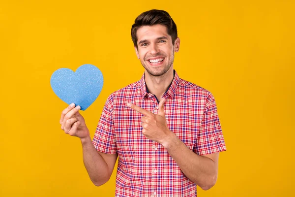 Portrait of attractive cheerful guy holding demonstrating blue paper card isolated over bright yellow color background — Fotografia de Stock