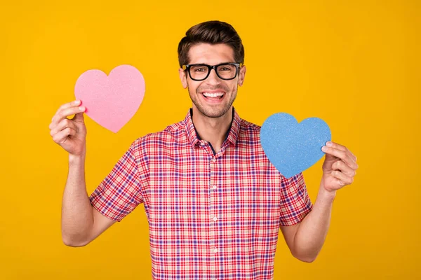 Portrét atraktivní veselý chlap drží v ruce dvě srdce znamení péče o lásku izolované přes jasně žluté barvy pozadí — Stock fotografie