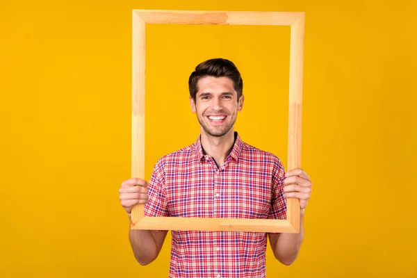 Фото веселого молодого счастливого человека, держащегося за руки деревянной рамкой улыбки изображение изолировано на желтом фоне — стоковое фото