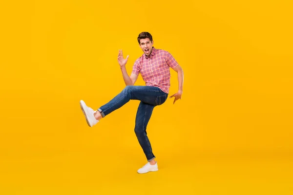 Foto de tamaño completo de feliz alegre loco hombre danza funky levantar la pierna divertido aislado en el fondo de color amarillo —  Fotos de Stock